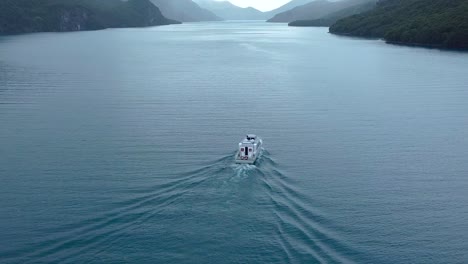 sailing across a blue lake under the rain, sorrounded by dense forests and snowy peaks patagonia, argentina