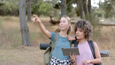 young caucasian woman points into the distance as a young biracial woman looks on, holding a tablet