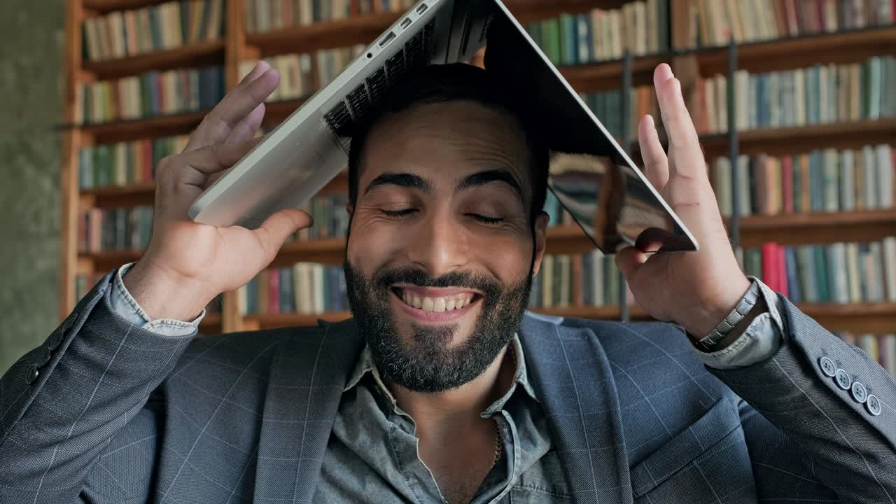 un tipo gracioso en la biblioteca con una computadora portátil sobre la cabeza.