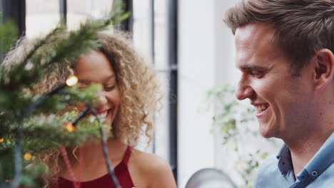 couple at home hanging decorations on christmas tree together