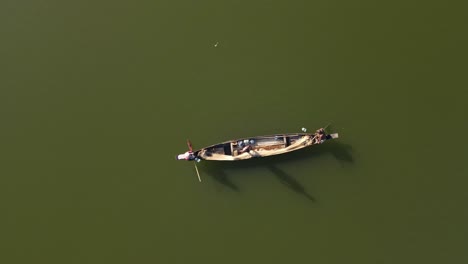 top down aerial shot of a small wooden boat in a lake and fishermen catching fish with net in traditional style