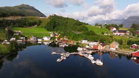 slow aerial trucking pan of beautiful norwegian fishing village with water reflecting green mountains and sky