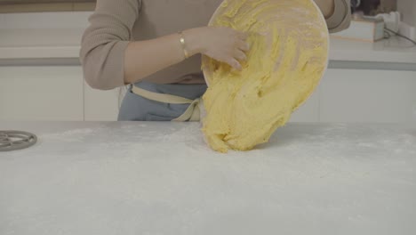 close up view of a lady pouring a sponge dough from a bowl onto a white table before baking in the kitchen.