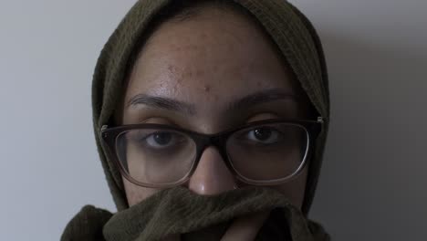 muslim female wearing glasses holding hijab covering her mouth looking at camera