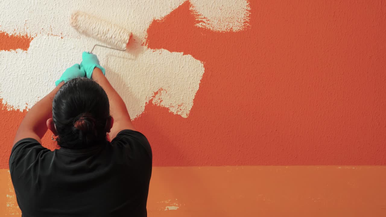 trabajador usando un rollo de pintura para pintar una pared naranja en color blanco