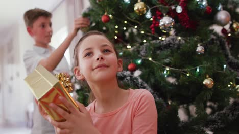 happy caucasian siblings decorating christmas tree at christmas