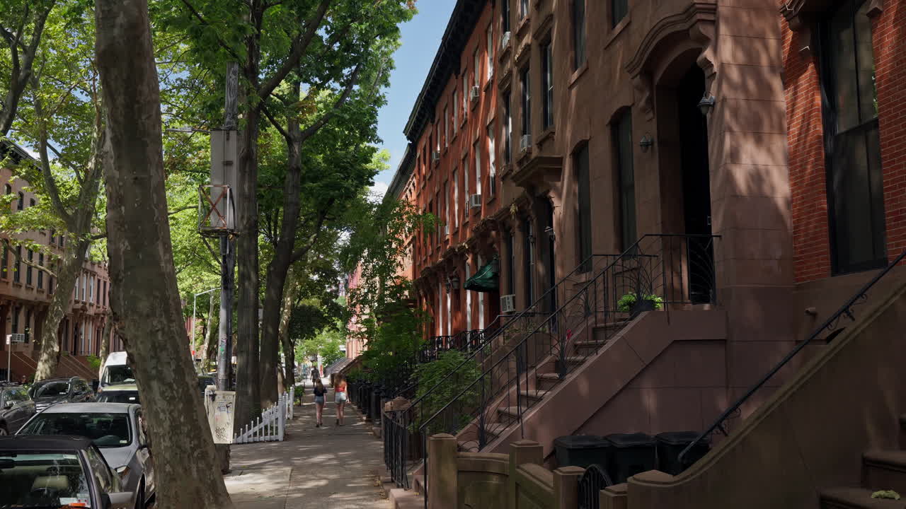 A serene summer day on Joralemon Street in Brooklyn, showcasing classic brownstone buildings and lush trees with two young women walking along the sidewalk.