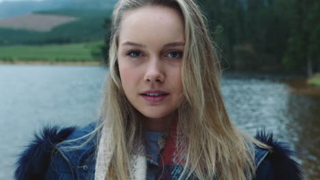 retrato de una hermosa mujer rubia con expresión seria en un frío día de invierno al aire libre junto al lago con el viento soplando el pelo 4k