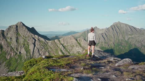 female hiker walking at headland with rocky hills in background during summer in norway. - static shot