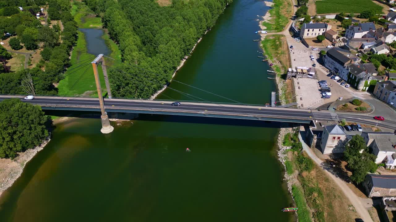 Drone top-down shot moving forward along Loire River, showing Saint-Florent-le-Vieil bridge, vehicles, village, and surrounding greenery - Mauges-sur-Loire in France