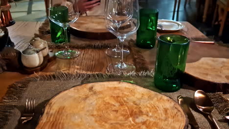 close-up of wooden plate chargers, green glasses, and wine glasses at a rustic-style restaurant in kuta selatan, bali, indonesia