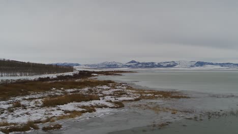 Ice-forms-along-the-shoreline-of-the-south-end-of-Utah-Lake-near-Lincoln-Beach,-looking-toward-the-west-mountains-as-seen-by-drone