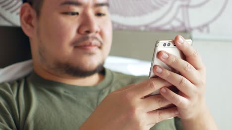 a young man use mobilephone for online shopping, chatting on the bed in bedroom