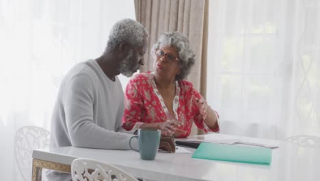 A-senior-African-american-couple-at-home,-working-on-papers-in-social-distancing