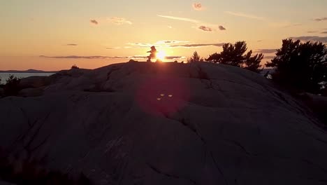 fly past inukshuk on rocky pine tree island at sunset, drone aerial wide dolly in