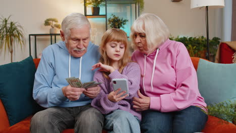 niña nieta con abuelos contando dinero usando una calculadora de teléfono inteligente en casa