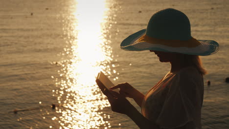 una joven con un sombrero usa una tableta contra el telón de fondo del sol naciente en una vista superior del muelle del mar