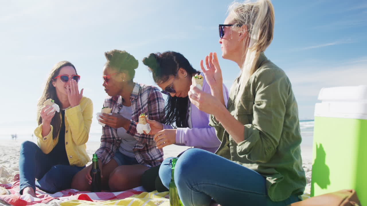 un grupo feliz de amigas diversas divirtiéndose, haciendo picnic en la playa