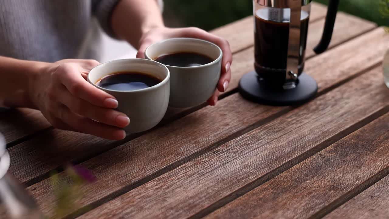Person holding two cups of coffee on a wooden table