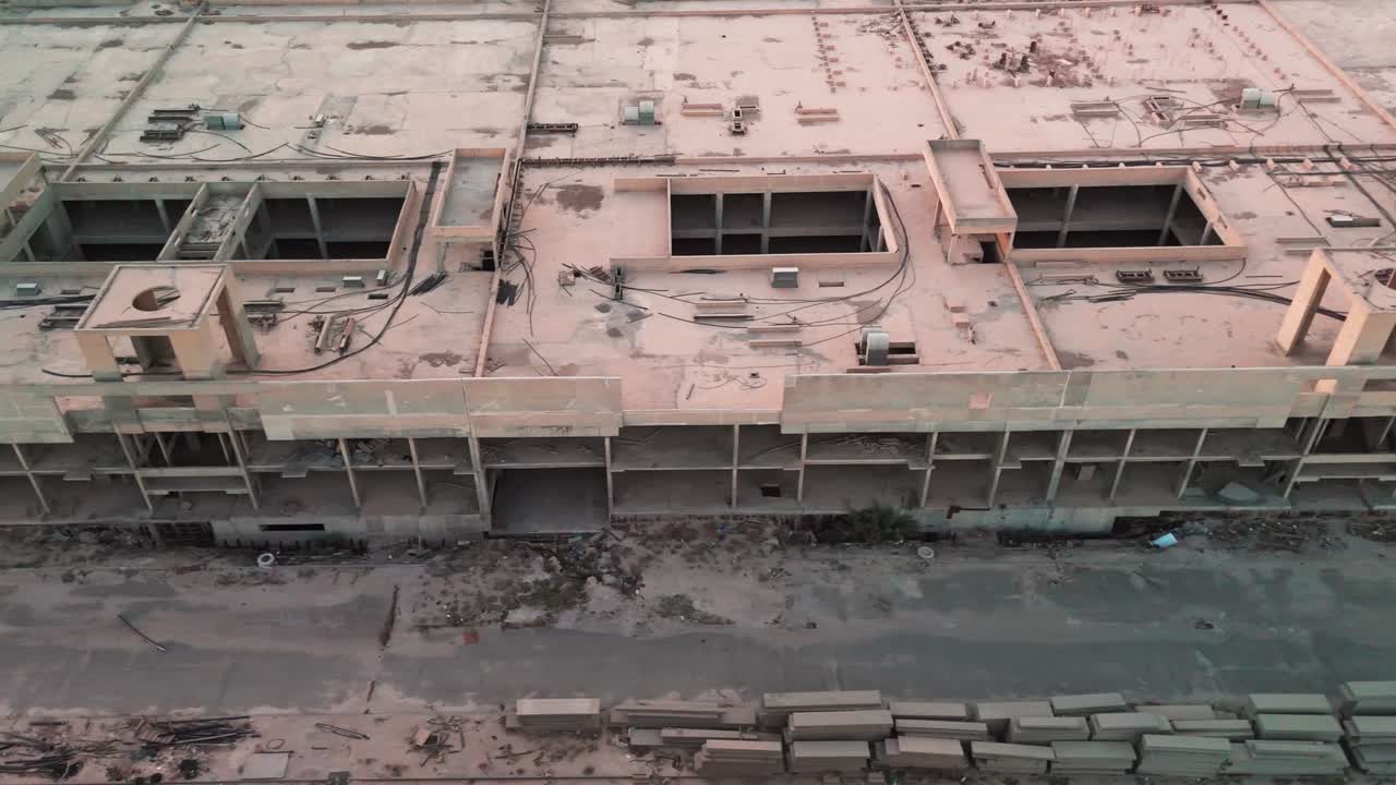 Vista aérea con dron de un complejo de hormigón inacabado con cableado en la azotea, huecos abiertos, pasillo vacío y escombros dispersos: solar en construcción abandonado ideal para temas industriales, de seguridad e inmobiliarios
