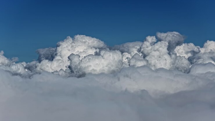 Massive white storm clouds floating above a soft cloud blanket against a deep blue sky