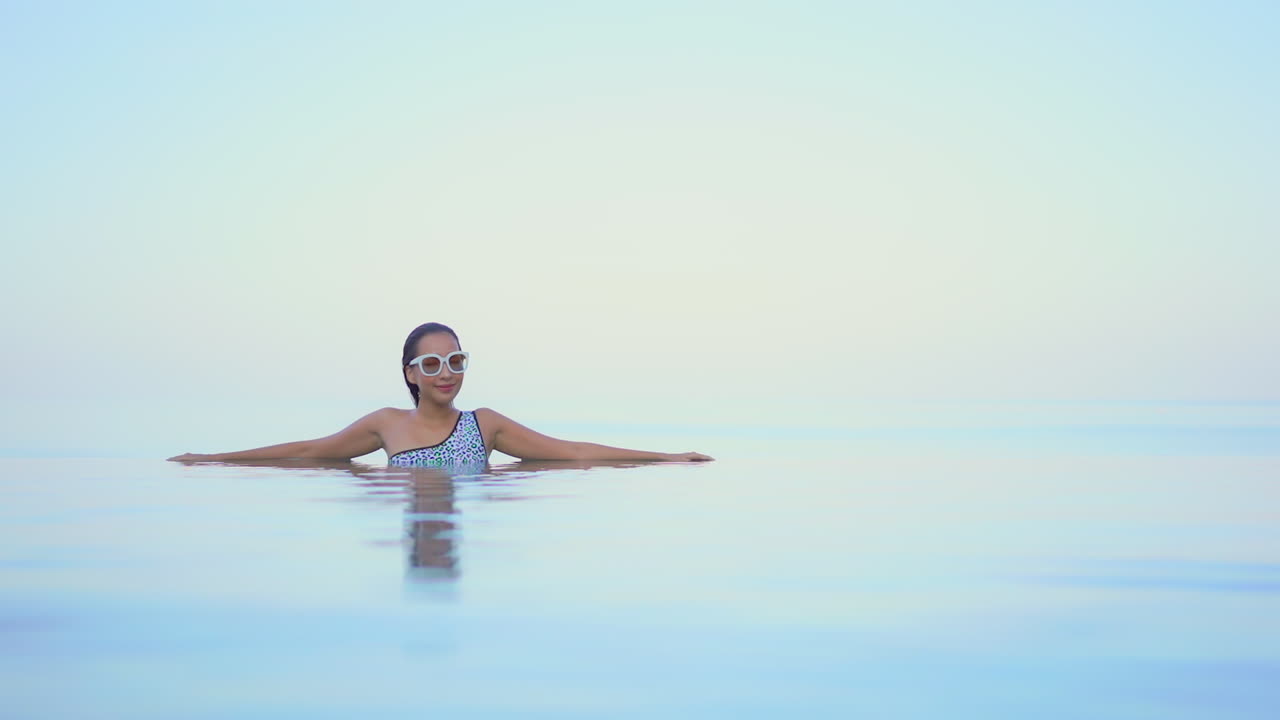 Eine Frau mit ausgebreiteten Armen am Rand eines Infinity-Pools scheint im Raum zu schweben vor einem Meereshorizont
