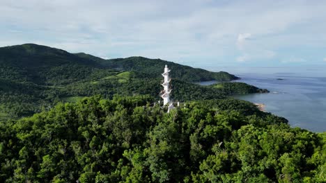 epic, aerial orbit view of bote lighthouse atop jungle-covered mountain with breathtaking island in background, showcasing lush rainforests, pristine ocean bays and idyllic mountains