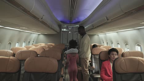 asian female flight attendant help service for african man customer keep suitcase to overhead luggage compartment on cabin airplane.