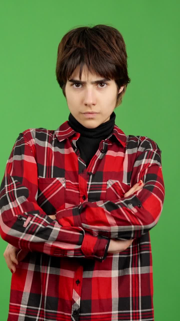 Young person with arms crossed and stern expression against green screen