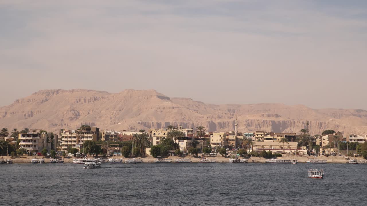 panorámica de barcos flotando a lo largo del nilo con montañas en el fondo en luxor, egipto