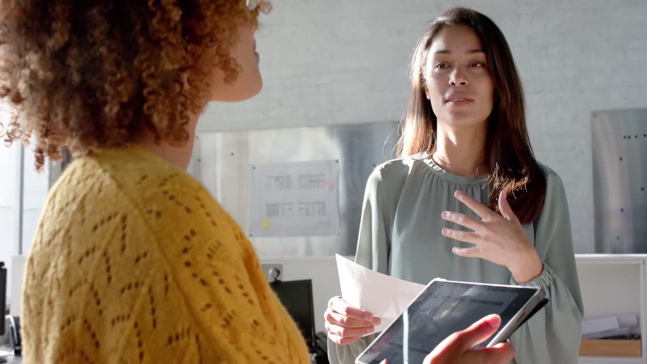 felices colegas femeninas diversas con tableta y documentos discutiendo el trabajo en la oficina, cámara lenta
