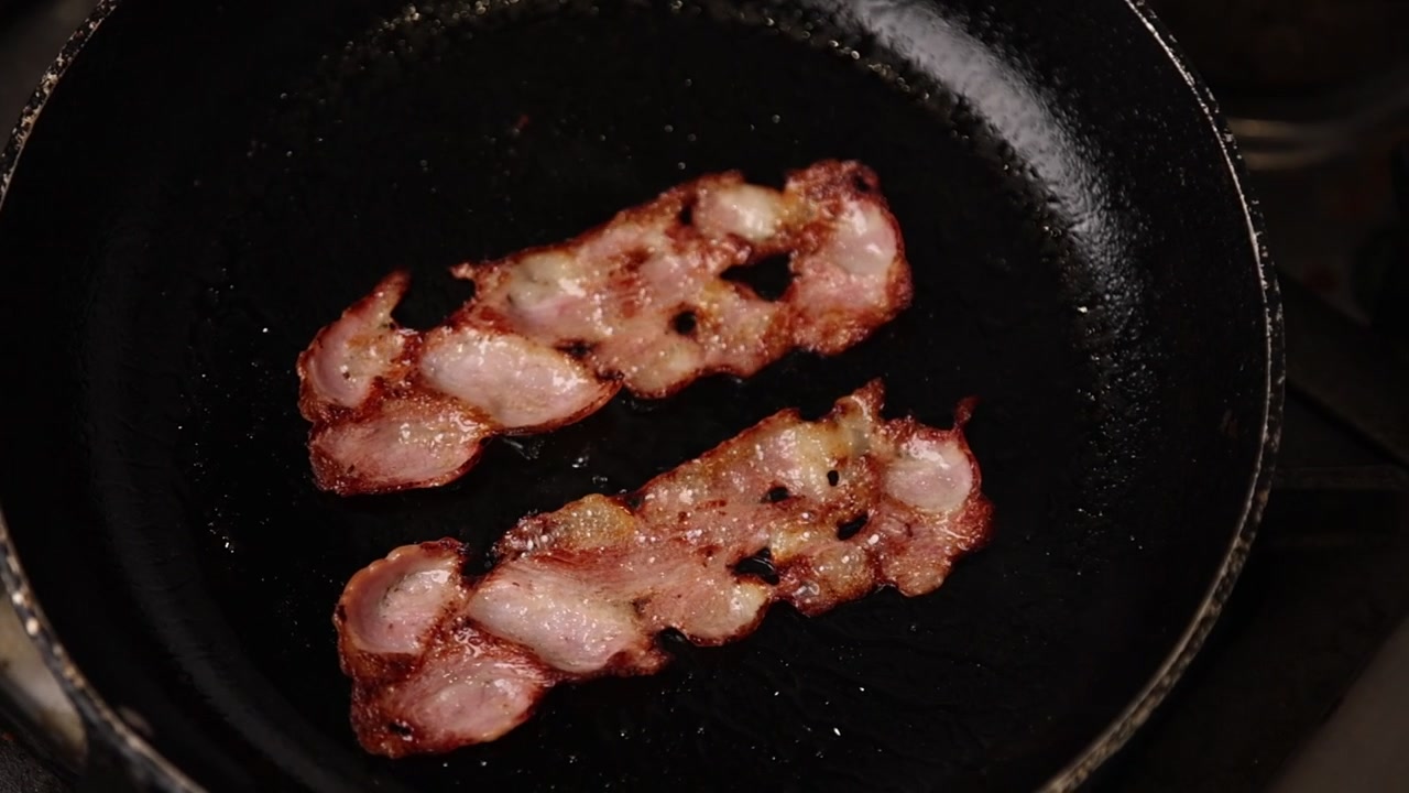 Due fette di pancetta che sfrigolano in una padella