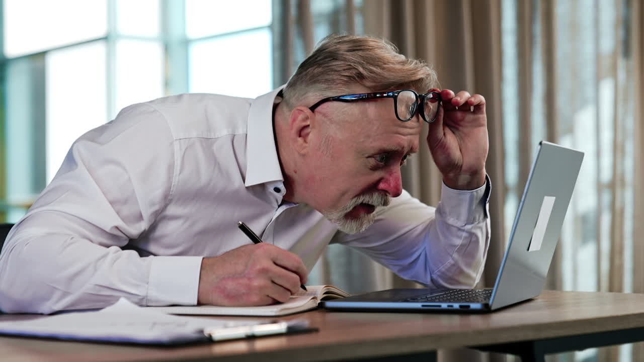Senior man with a bad sight puts off his glasses approaching close to the computer screen. Puzzled man looking surprised from what he read at the laptop.