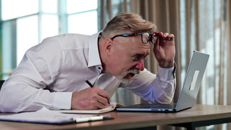 senior man with a bad sight puts off his glasses approaching close to the computer screen. puzzled man looking surprised from what he read at the laptop.