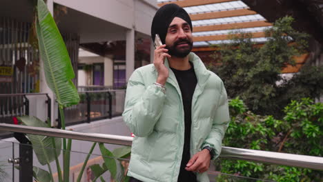 indian man in turban leaning on railings talking happily on the phone