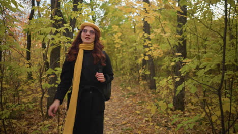 lady in yellow beret, and backpack holding bag strap while walking through an autumn park filled with tall trees and dry foliage, sunlight creating a warm effect as she focuses on her journey