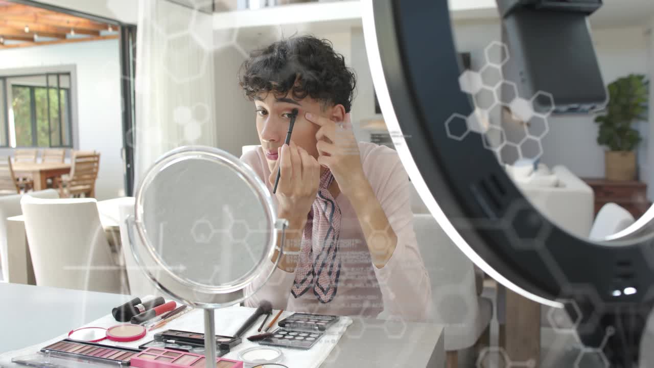 Male creator applying eye makeup for camera, phone filming, hexagon overlay obscuring reflection