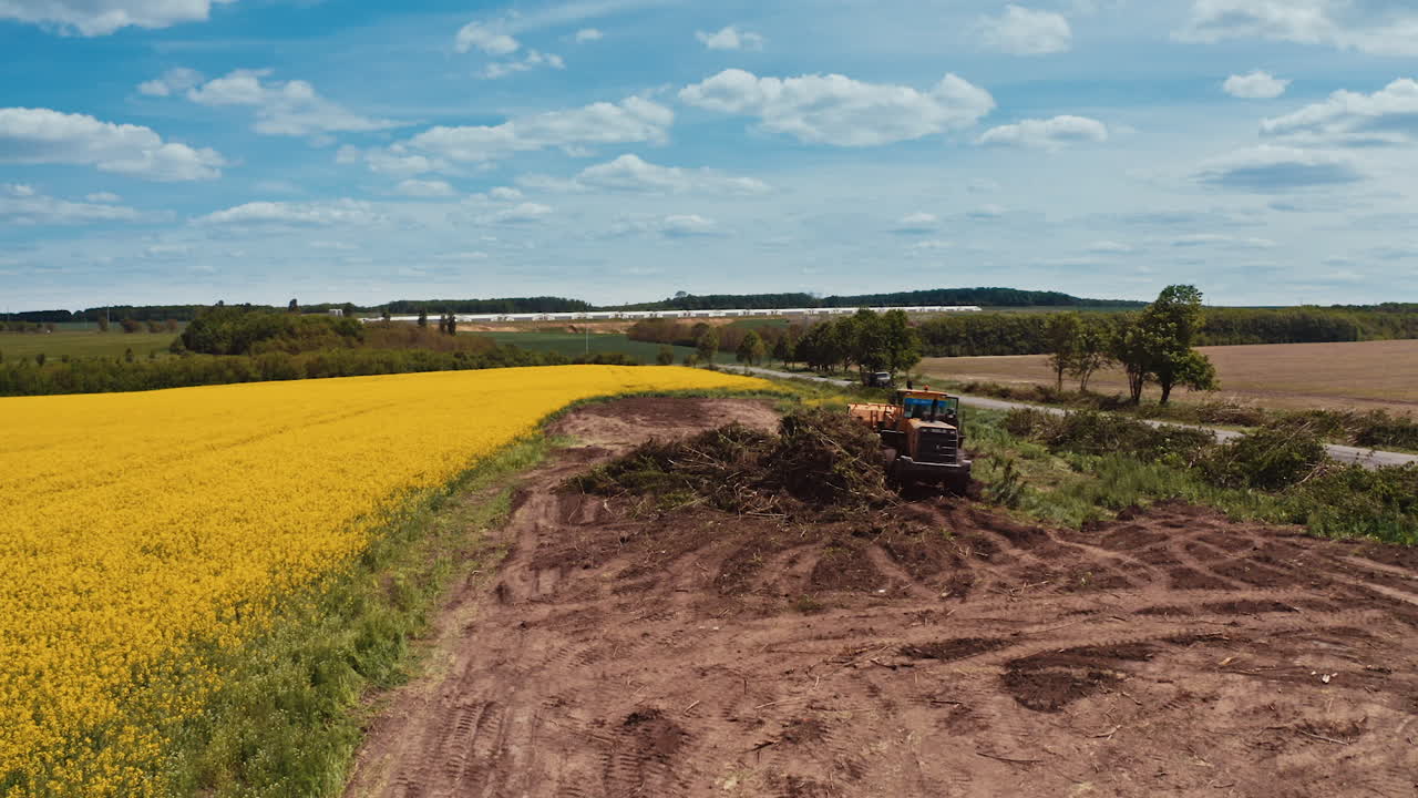 Tractor working on the field. Agricultural machine among nature. Yellow field in the countryside in summertime.