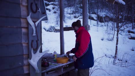man pouring hot water dishwashing liquid into basin to clean knife on a winter day