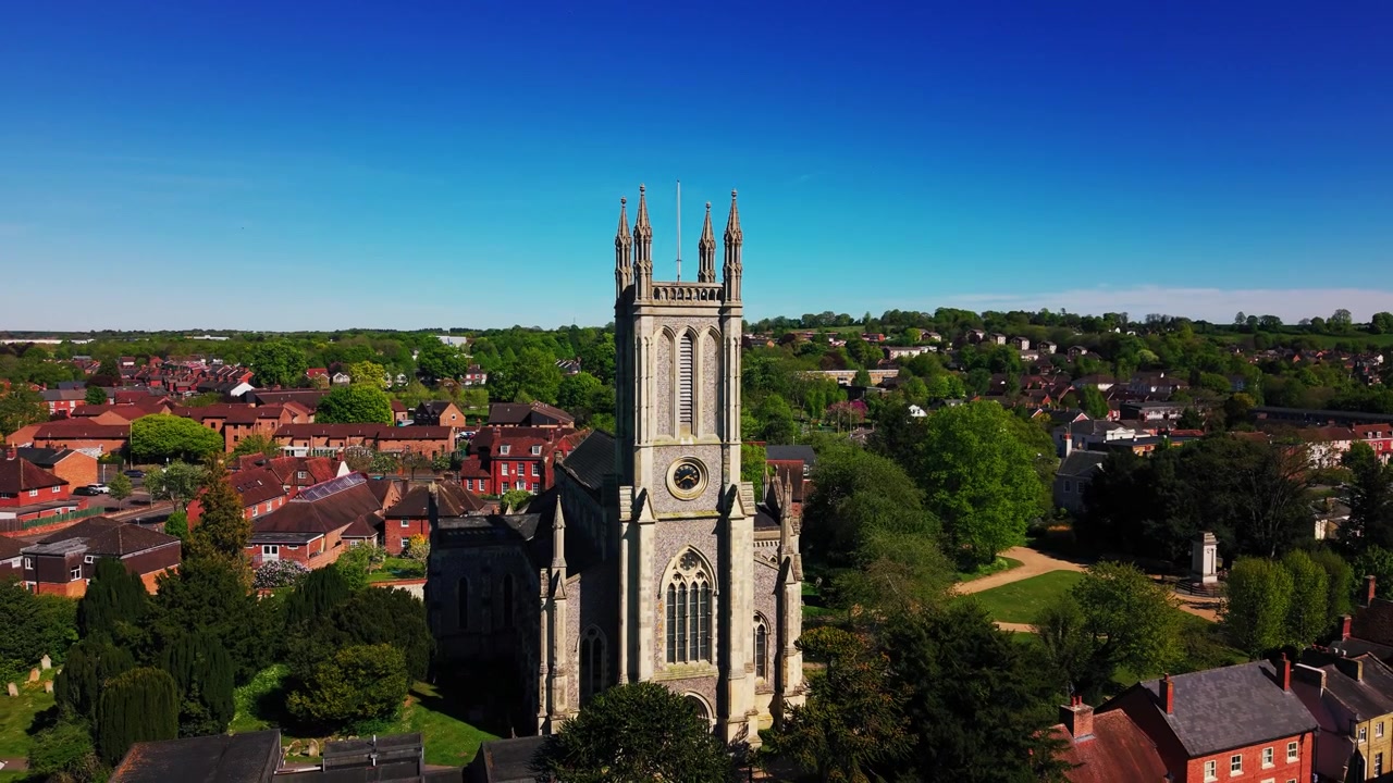 Riprese aeree ravvicinate con drone della torre della Chiesa di Santa Maria ad Andover contro un cielo azzurro limpido. La ripresa mostra l'architettura storica della chiesa, la torre in pietra, il quadrante dell'orologio, gli alberi e i tetti circostanti