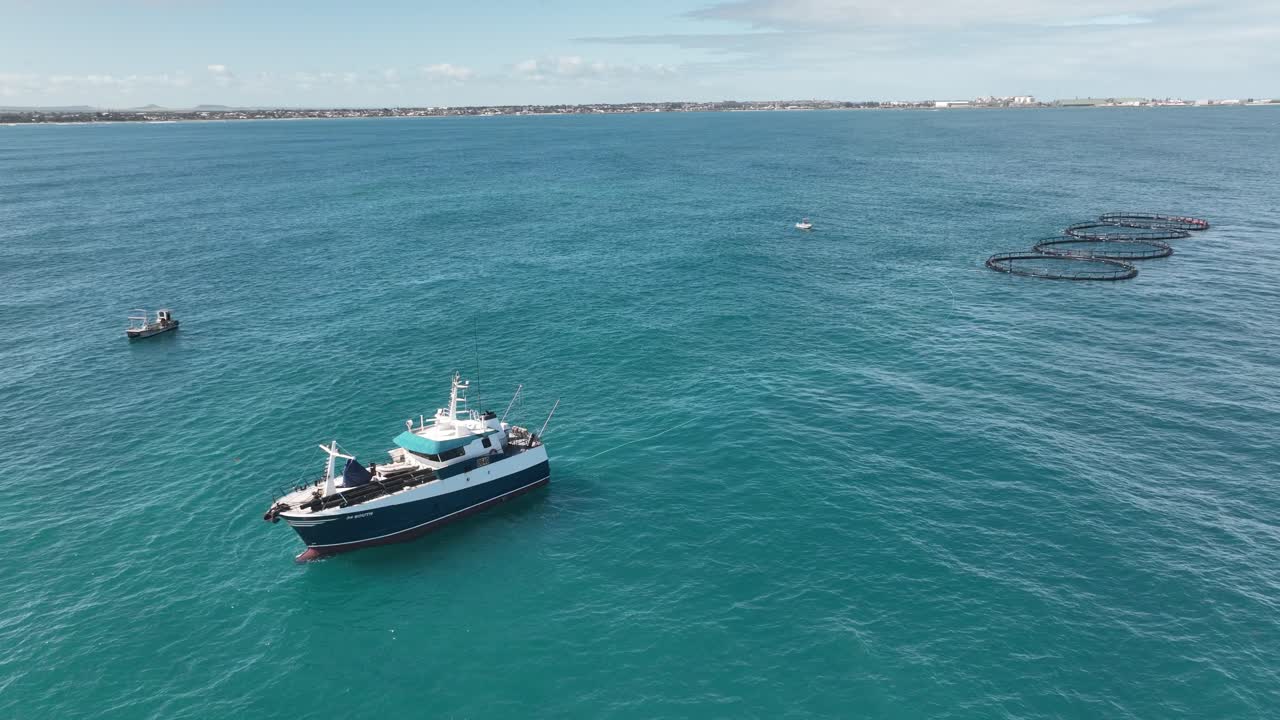 un buque marino de tamaño mediano remolca cuatro granjas de peces a lo largo de la costa occidental de australia.