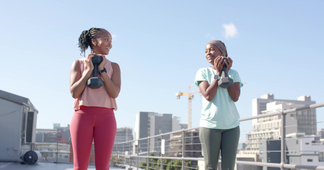 Amiche africane che vedono manubri esagonali, camminano, si piegano, sollevano e tengono i pesi per un allenamento sul tetto
