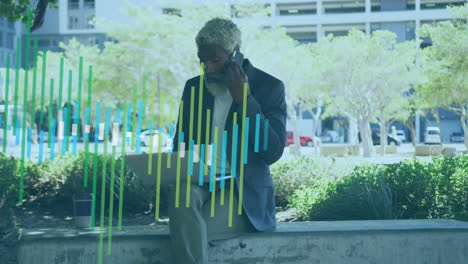 animation of graphs over african american man working on laptop while talking on cellphone