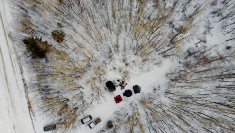 aerial birds eye view rise over winter camping with tents forming a v with a campfire dogs entertained on a sunset with bare trees tipped in golden yellow off a snow covered backroad on crown land 3-3