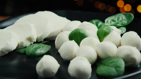 pequeñas bolas de queso mozzarella blancas, hojas de espinaca en un plato negro.