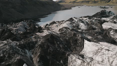 low flyover above rugged surface of iceland glacier towards lake, mountain range