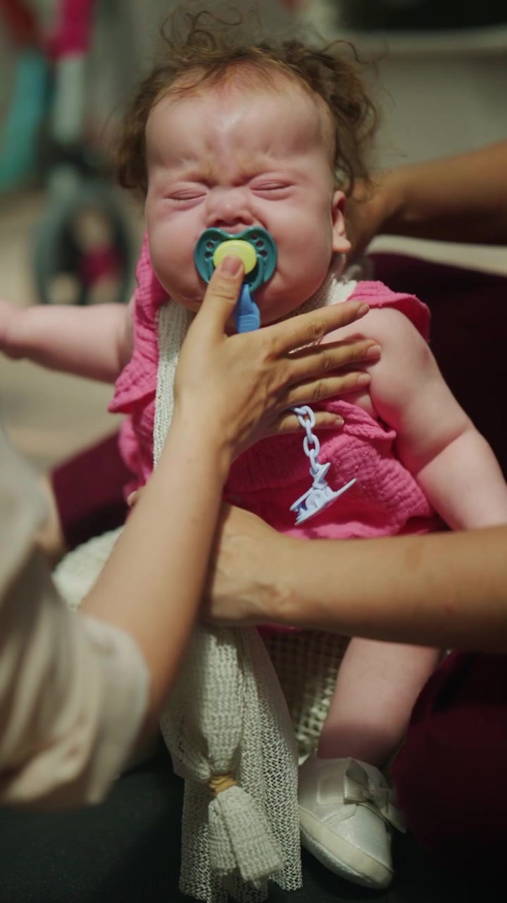 Close up of an infant resting in a supported position while the mother places a pacifier in the baby's mouth during a pediatric mobility and developmental therapy session