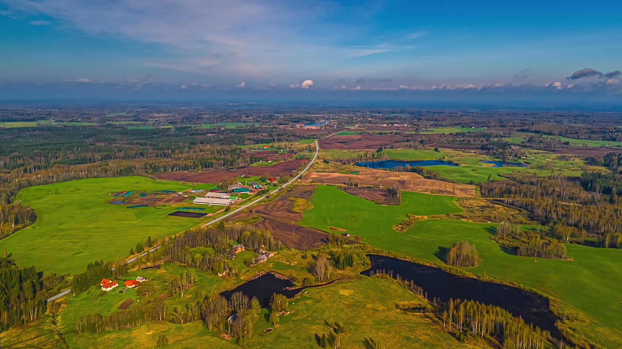 Green Earth landscape and rural farmland fields, meadows, forests, and ponds below a flowing cloudscape time lapse