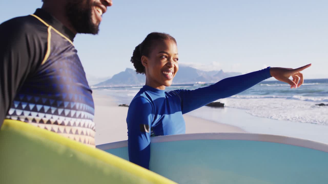 African american couple talking and carrying surfboards on the beach