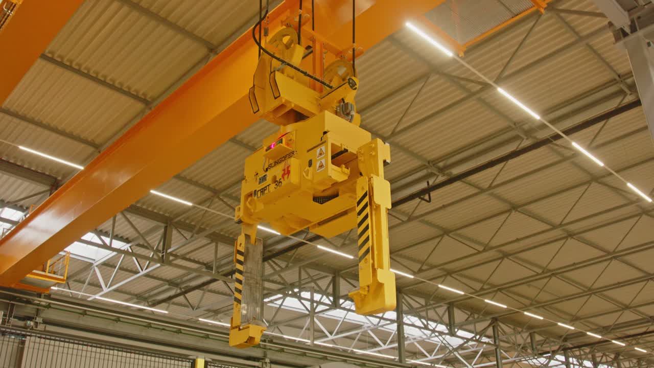 A large clamp crane in a big factory goed down and grabs a heavy steel coil
